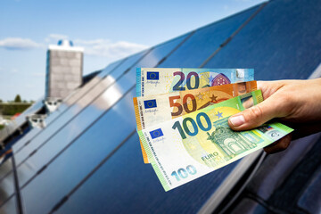 Euro banknotes held in a hand, with solar panels on a house in the background
