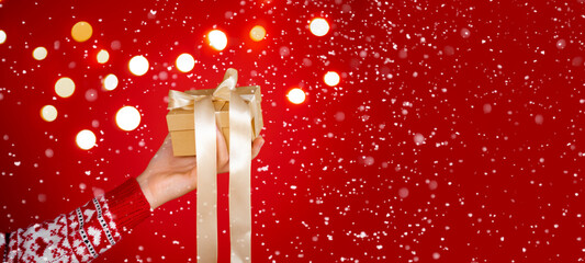 Girl hands holding christmas gift on red background with snow. Christmas banner. Minimalism....