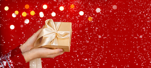 Girl hands holding christmas gift on red background with snow. Christmas banner. Minimalism....