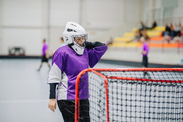Close-up of woman floorball goalkeeper in helmet concetrating on game in gym.