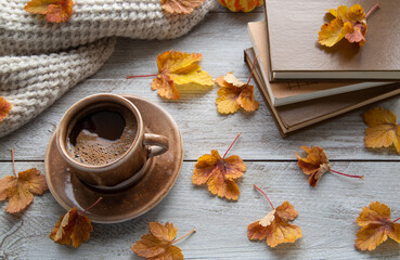 Autumn mood, autumn atmosphere. A cup of coffee, a knitted scarf, books and autumn leaves on the...