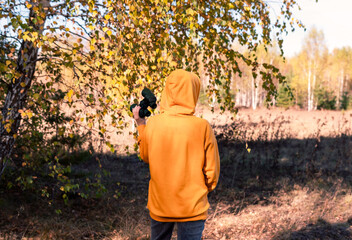 rear view of Young woman in yellow sweatshirt and hood with binoculars watching birds in the autumn forest Birdwatching, zoology, ecology Research, observation of animals Ornithology