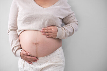 The mature Asian woman stood on the white backdrop, gracefully unveiling her large round belly, cradling it with both of her hands.