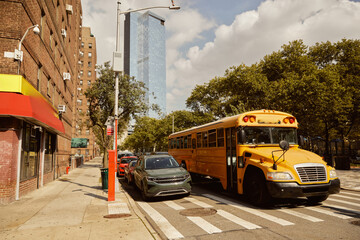 Obraz premium yellow school bus and cars on crosswalk near trees with fall foliage in new york city, autumn scene