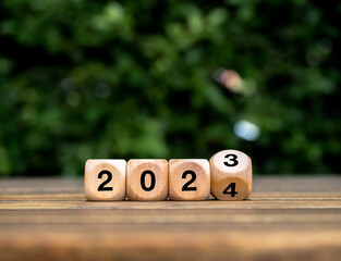 Happy new year 2024 with start new story, trends and business. Environmental sustainability concepts. Flipping 2023 to 2024 numbers on eco wooden cube blocks on wood table, green leaves background.