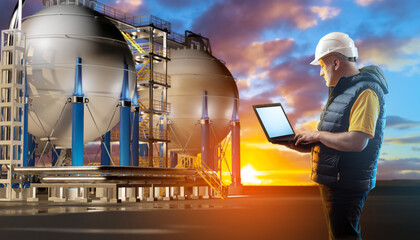 Oil worker near BPVC tanks. Man with laptop near factory. Oil worker guy at work. Spherical high pressure tanks at sunset. Oil worker watches working at fuel factory. Career in petroleum industry