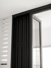 Close-up door hinges on the black aluminum folding doors with glass on white building background, vertical style.