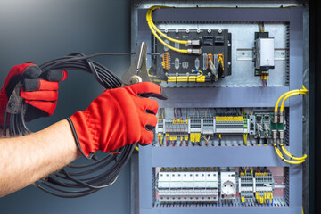 Electrician hands. Power shield. Electrical cabinet. Electrician cuts wire. Power panel on wall. Repair of electrical equipment. Power shield with machine guns. Electrician hands with pliers