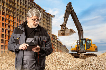 Man builder. Crawler excavator at construction site. Gray-haired worker near unfinished house....