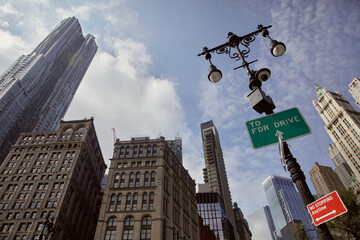 street pole with lanterns and traffic signs against skyscrapers in new york city, low angle view