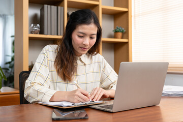 Fototapeta na wymiar young asian woman Taking online meeting notes on paper to make them easy to remember and review. Working from home happy with work Be diligent in work