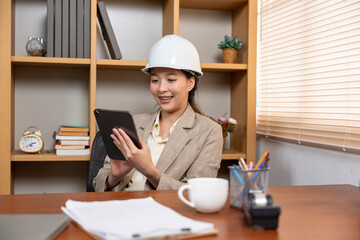 A female engineer is giving orders via a tablet. With a smiling, happy face Because work is smooth as desired
Order work online Sip coffee while working - obrazy, fototapety, plakaty