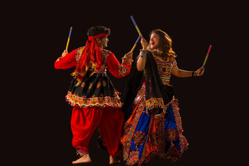 A  happy young couple performing Dandiya Raas on a black background, during Navratri celebrations