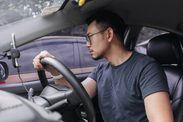 Asian Thai man with beard,  wear eyeglasses parking a car, looking at car side mirror while driving training.