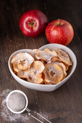 in the foreground a bowl with slices of homemade dried apple flavored with icing sugar