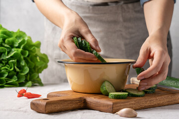 Women folding cucumber into salad bowl. Cooking healthy food close up view