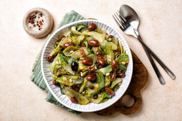 Italian salad made with sauteed broad-leaved endive or escarole with taggiasca olives, pine nuts, raisins. Vegan dish. Top view. - obrazy, fototapety, plakaty