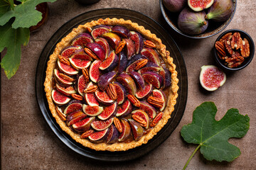 Top view of California Fig and Bourbon Pecan Pie or tart, homemade pie crust with figs, brown sugar, butter, eggs and pecans filling, decorated with fresh figs and  toasted pecan. Brown table. - obrazy, fototapety, plakaty