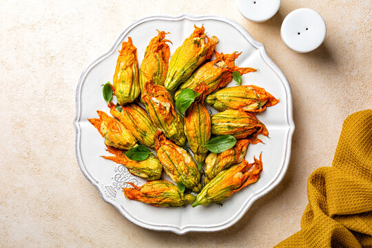 Zucchini Flowers stuffed with ricotta cheese, egg and bread crumbs, parsley. Oven baked courgette or pumpkin flowers. Italian dish fiori di zucca on a white plate.
