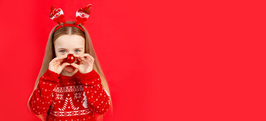 a child girl in a sweater with a ball on her nose on a red monochrome isolated background rejoices...