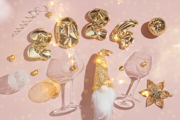 Happy New Year festive background, golden inflatable balls in shape 2024 on pale pink background, sparkling wine champagne bottle, wine glasses with Christmas holiday shiny decor, glitter