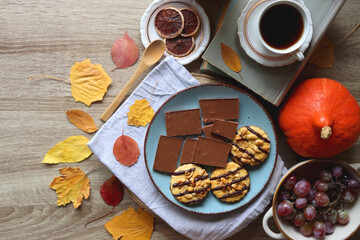 Cup of tea or coffee, plate with cookies and chocolate, dried oranges, bowl of grapes, vintage books, pumpkins and autumn leaves on the table. Autumnal hygge. Top view.