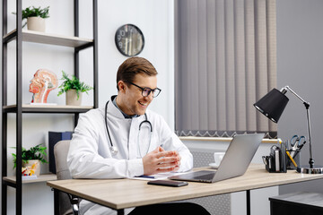 Portrait of man doctor talking to online patient on laptop screen sitting at clinic office desk giving online consultation for domestic health treatment. Telemedicine remote medical appointment