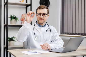 Young attractive doctor otolaryngologist sitting at his workplace in the office and holding an ear...