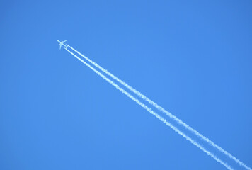 Large two engine passenger supersonic airplane flying from right to left high in blue cloudless sky leaving long white track