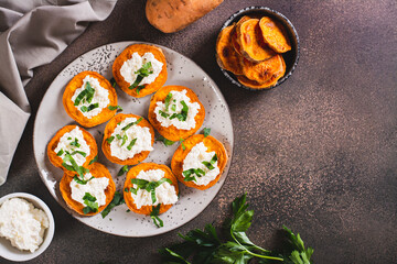 Pieces of baked sweet potato with ricotta and herbs on a plate on the table top view