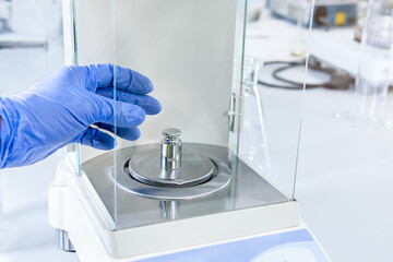 A operator's hand is holding steel calibration weight to place on the analytical balance. Concept...