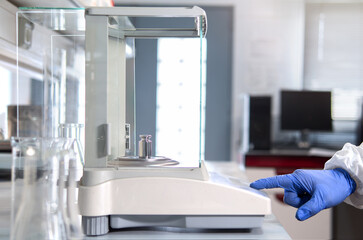 A operator's hand is holding steel calibration weight to place on the analytical balance. Concept...