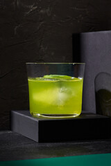 A basil-flavored gin and tonic elegantly presented on a podium, capturing minimalist bar artistry against a deep black canvas