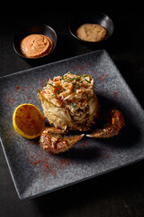 Delicately cleaned crab meat paired with lemon, served in a crab with claws and two types of sauce, against a dark background with a low-key photography style