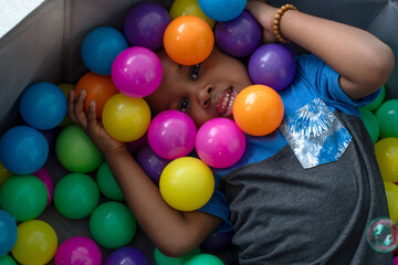 Fototapeta na wymiar Top view, portrait of African child boy in ball pit smiling at camera, playing with colorful plastic balls in ball pool