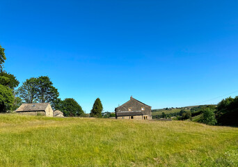 Fototapeta na wymiar Landscape, with long grass, stone buildings, trees and hills, set against a vivid blue sky in, Ripponden, UK