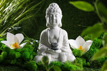 Buddha statue, stones, flowers and grass on green background, close up