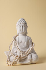 White Buddha statue and beads on light beige background