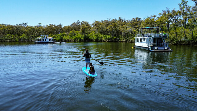 People on paddle boards on Blackwood River with houseboats in the background, Western Australia,