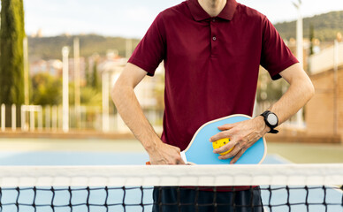 Head-on view of an unrecognizable senior male in sportswear poses with a pickleball racket and ball. Pickle ball advertising concept. Older men playing pickleball.