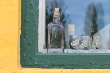 alte Flasche mit Gläsern hinter einer Scheibe eines alten Hauses