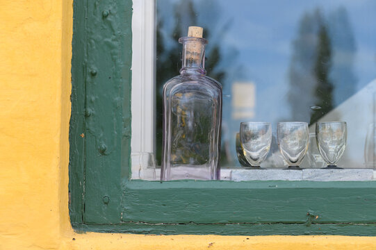 alte Flasche mit Gl&auml;sern hinter einer Scheibe eines alten Hauses