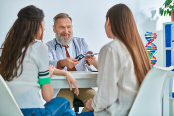 Obraz premium cheerful grey bearded doctor showing lgbt couple their ultrasound, in vitro fertilization concept
