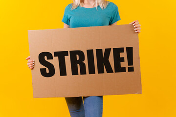 A woman protesting holding a sign with the slogan of the hollywood actors and writers strike on a yellow background