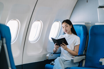 Smiling Asian woman enjoying reading a book comfortable flight while sitting in the airplane cabin, Passengers near the window.