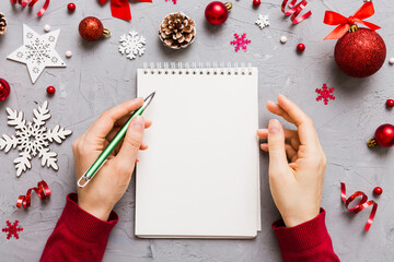 Woman writing Christmas to do list on notebook on colored background with xmas decorations