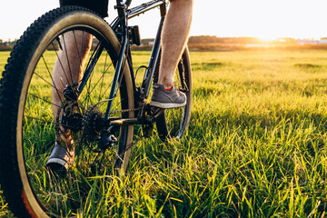 Close up of bicycle wheel off road at sunset time. low angle view of cyclist riding mountain bike. Healthy lifestyle and outdoor adventure concept - obrazy, fototapety, plakaty