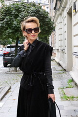 Dojrzała, elegancka kobieta na miejskim spacerze.
Kobieta w czerni. 