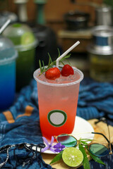 Iced strawberry soda and lemon, a refreshing drink, placed on a classic wooden table decorated with lemon petals and various fruits.
