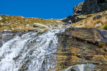 Escursionista attraversa un guado sopra la cascata ai Laghi del Paione, Val Bognanco, Verbano-Cusio-Ossola